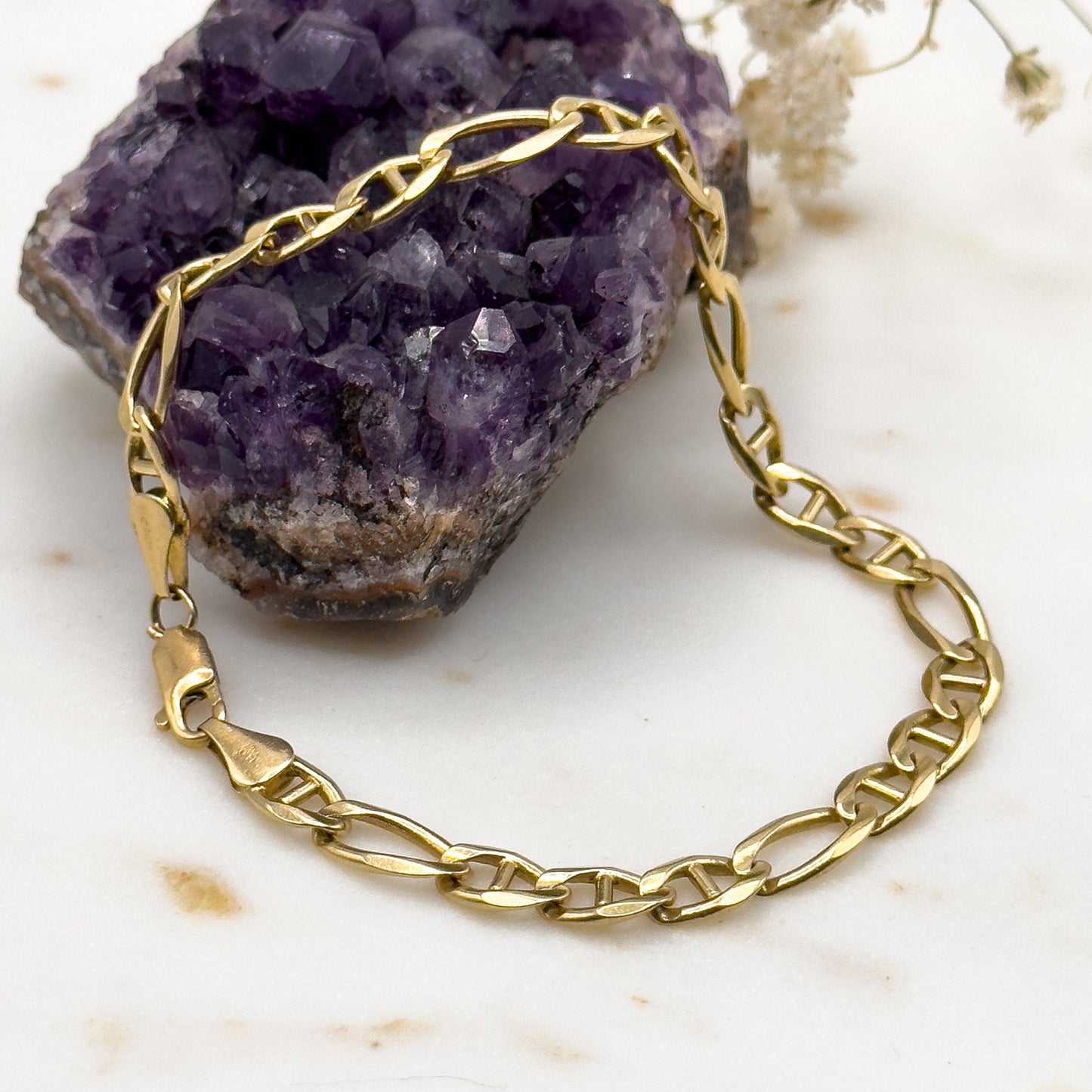 Gold chain bracelet on a purple crystal with white flowers