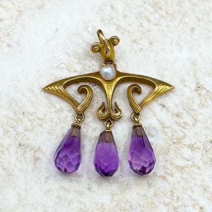 Gold pendant with purple teardrop-shaped gemstones on a textured white surface