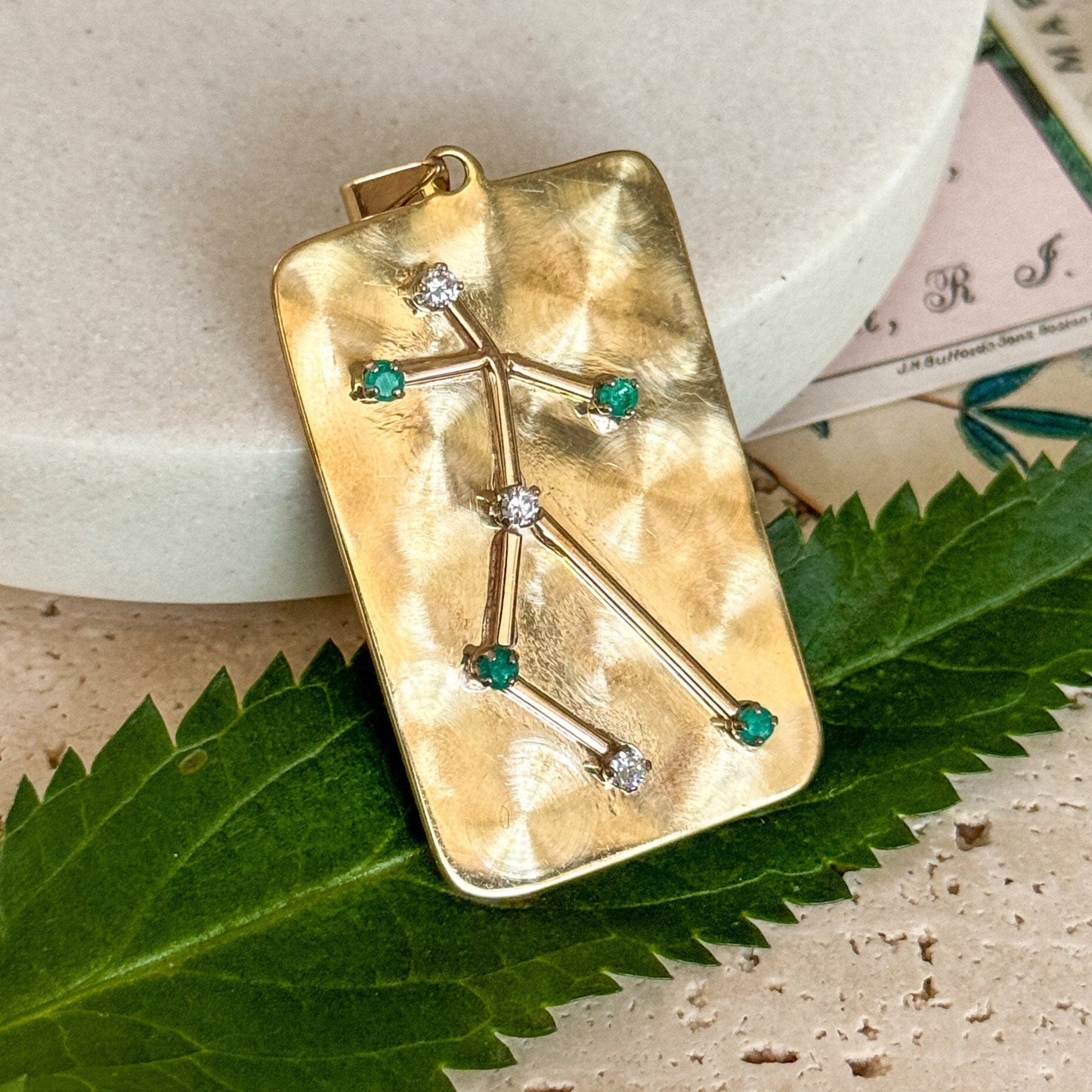 Gold pendant with green gemstones on a leaf