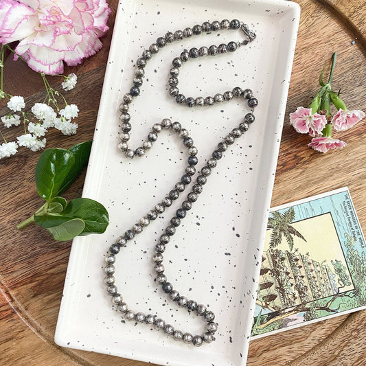 Necklace on a white dish with flowers and a postcard on a wooden surface