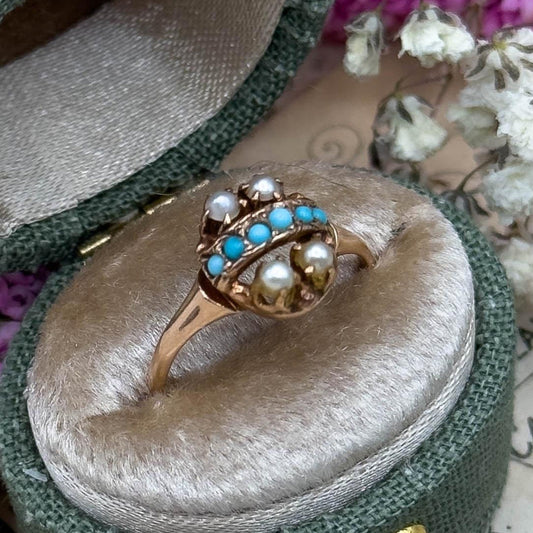 Gold ring with turquoise and pearl stones in a green velvet box on vintage paper with flowers.