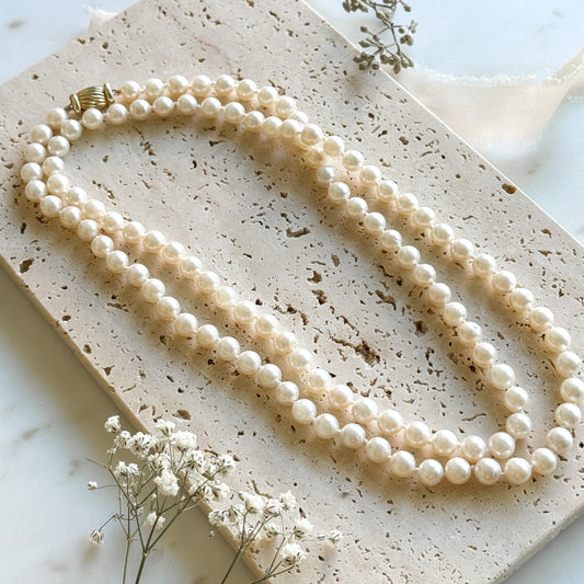 Pearl necklace on a textured stone surface with small white flowers.