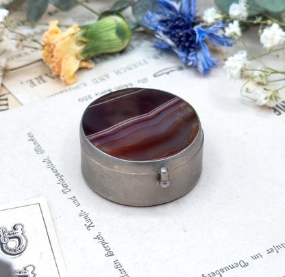 Round agate stone in a metal box on a newspaper background with flowers.