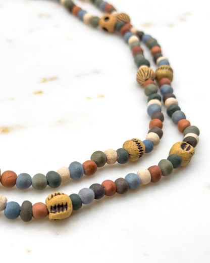 Two doubled strands curving side by side across pale marble, the near beads sharp and the far ones softening into blur, with notched ochre beads sitting at intervals along each row.