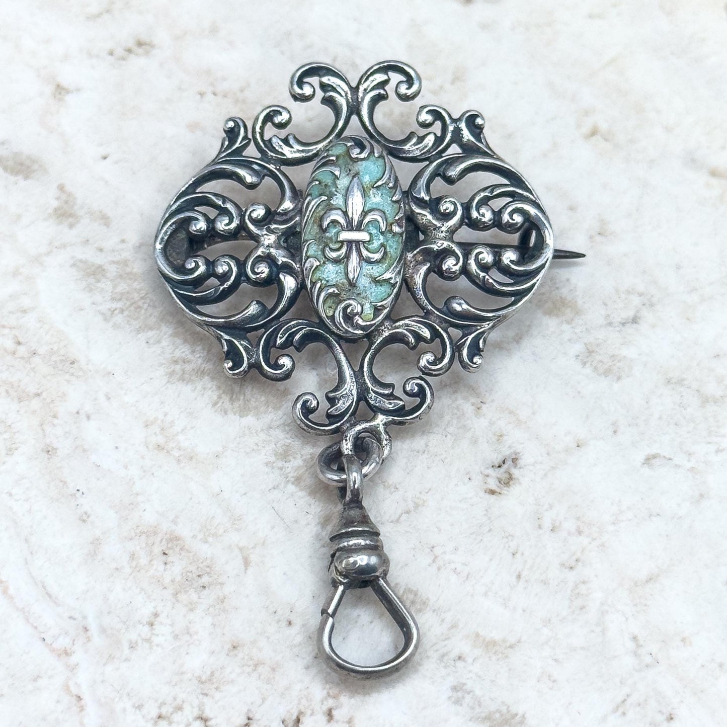 Decorative silver brooch with a central gemstone on a textured white background