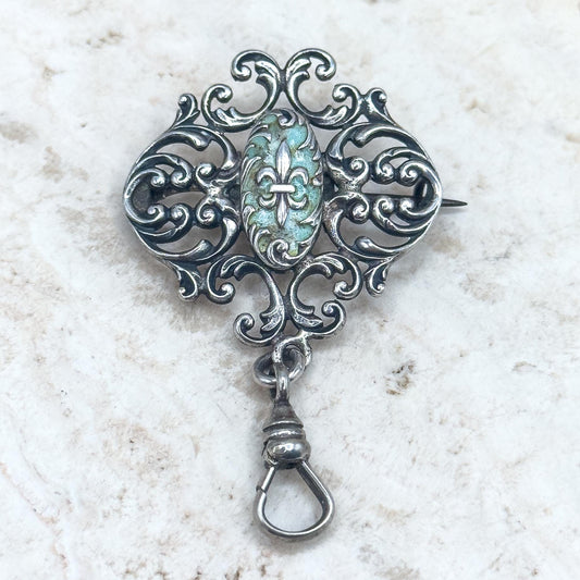 Decorative silver brooch with a central gemstone on a textured white background