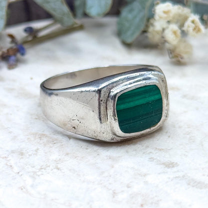 Silver ring with a green stone on a textured surface with plants in the background