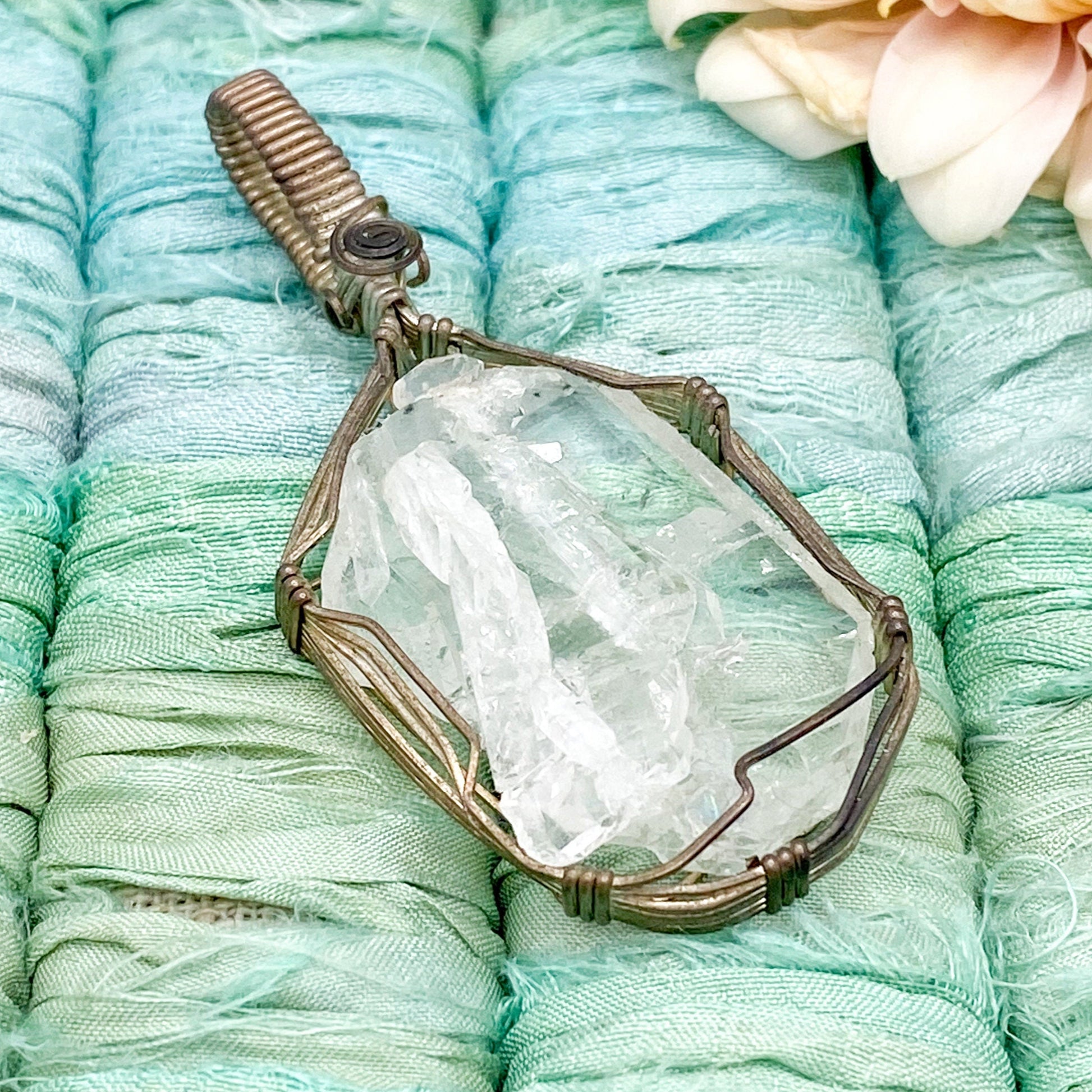 Crystal pendant on turquoise fabric with a flower in the background