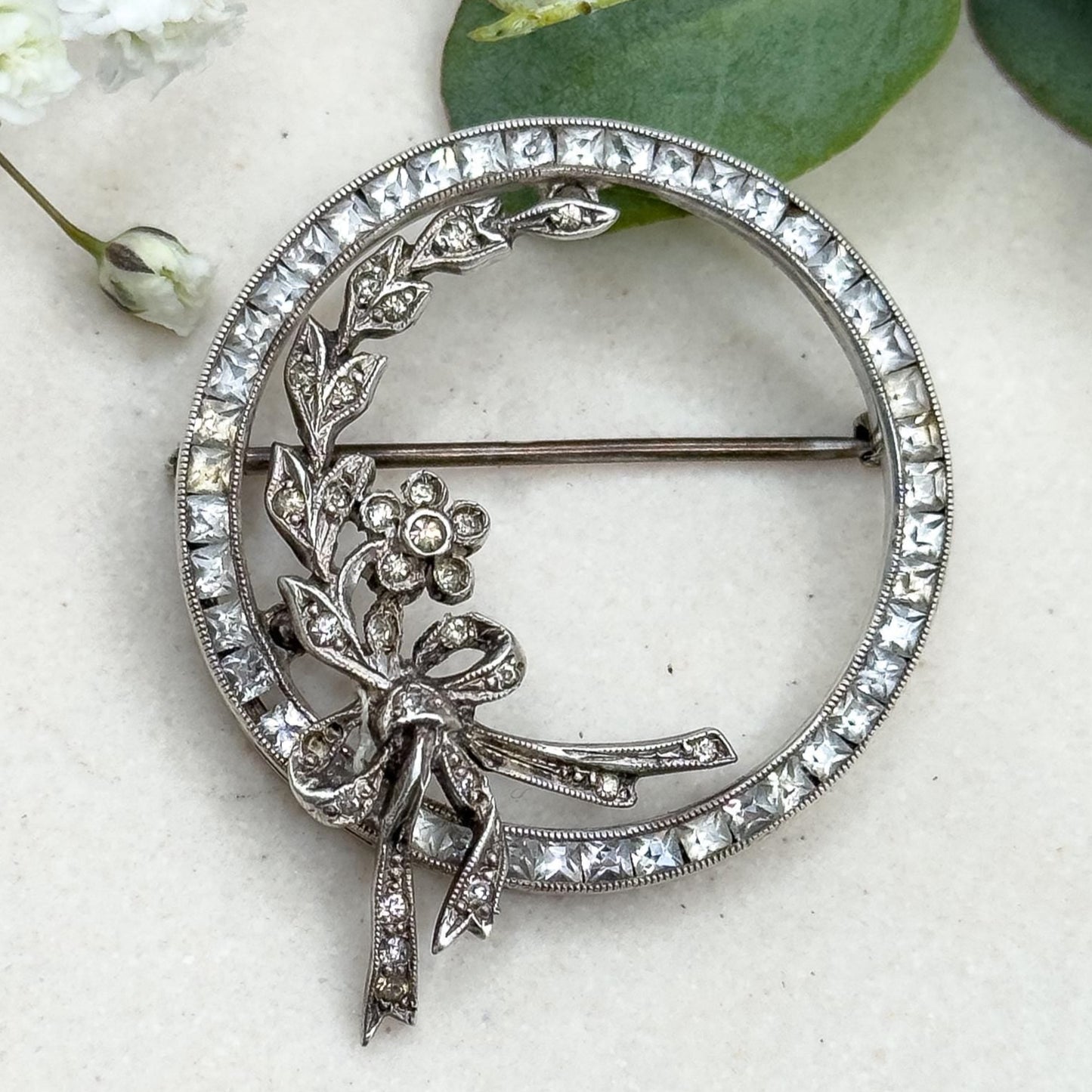 Silver brooch with floral design on a light background with greenery