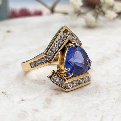Gold ring with a blue gemstone on a marble surface with white flowers in the background
