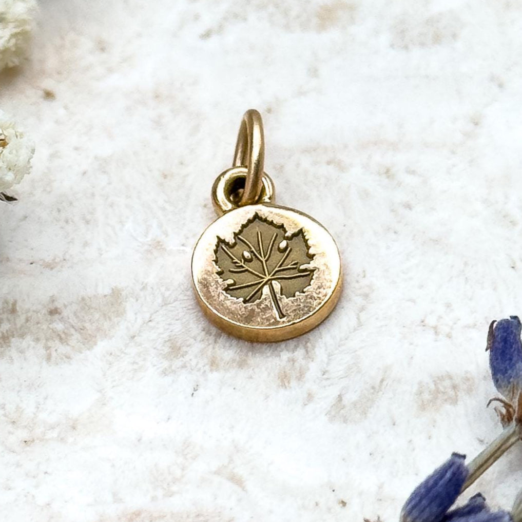 Gold pendant with a leaf design on a light background with white flowers and lavender.