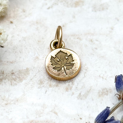 Gold pendant with a leaf design on a light background with white flowers and lavender.