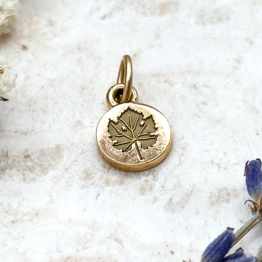 Gold pendant with a leaf design on a light background with white flowers and lavender.