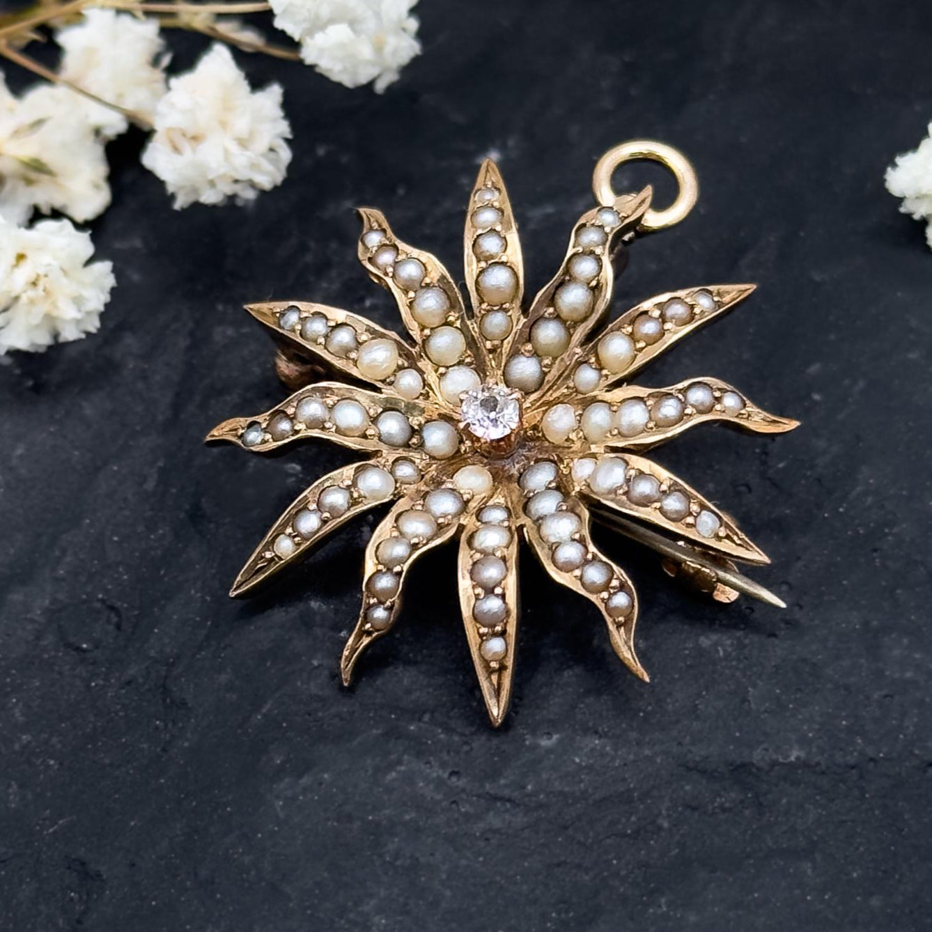 Gold star-shaped brooch with pearl-like stones on a dark surface with white flowers.