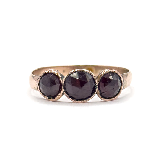 Almost the same view with slightly different angle, cropped in close so the three garnet domes and their yellow gold bezel rims fill the frame above the arching band.