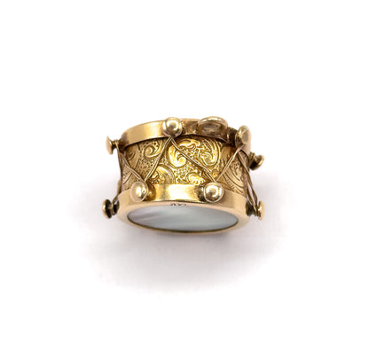 Tipped forward so the drum is viewed from slightly below, revealing the second mother of pearl face on the underside rim while the scrolling engraved side fills the centre.