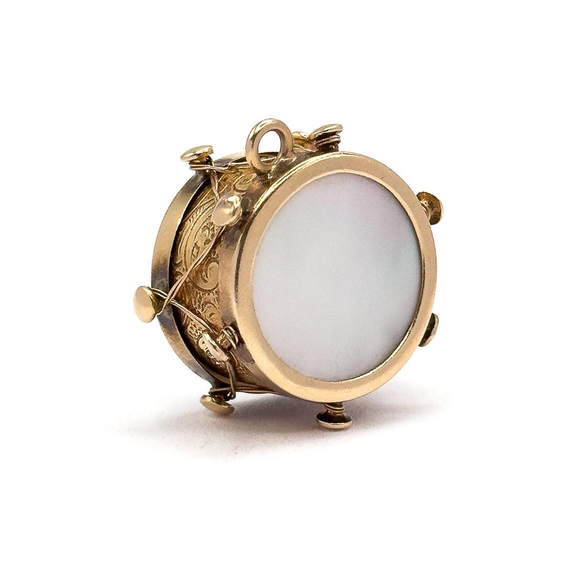 Angled three-quarter view with the charm standing on its lower knobs, one mother of pearl face turned to the right and the engraved side with its zigzag gold thread at the left.