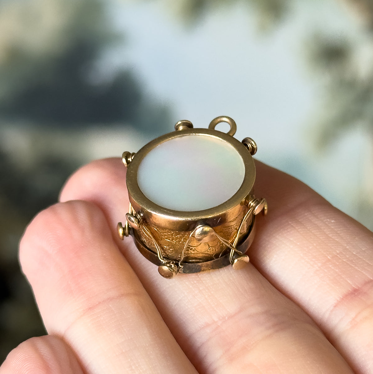 Angled closer on the fingers so the drum's engraved side band, zigzagging gold tensioning thread and small round knobs are visible below the mother of pearl face.