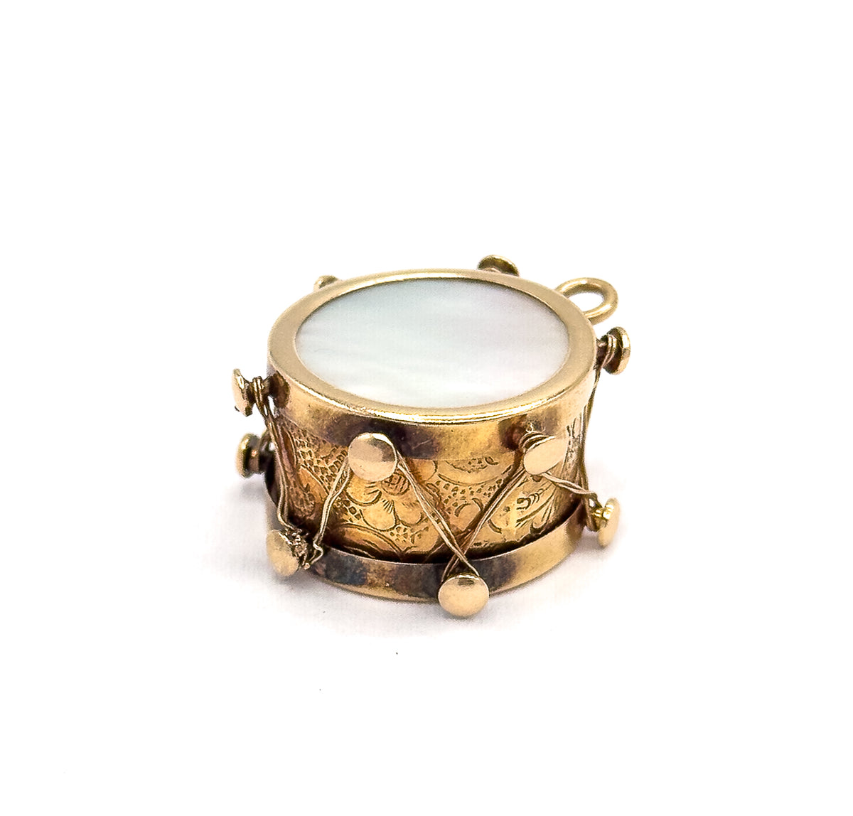 Off the hand now on a plain white background, tilted to show the whole round mother of pearl face, the scroll-engraved side with its gold thread and knobs, and the small bail at the upper right.