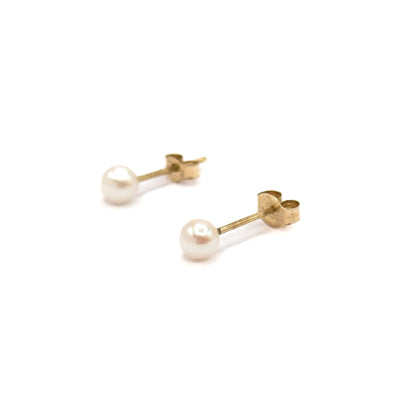 The pair set wide apart on a plain white ground, one stud higher than the other, with the flat face of each yellow gold butterfly back turned toward the camera behind its round white pearl.
