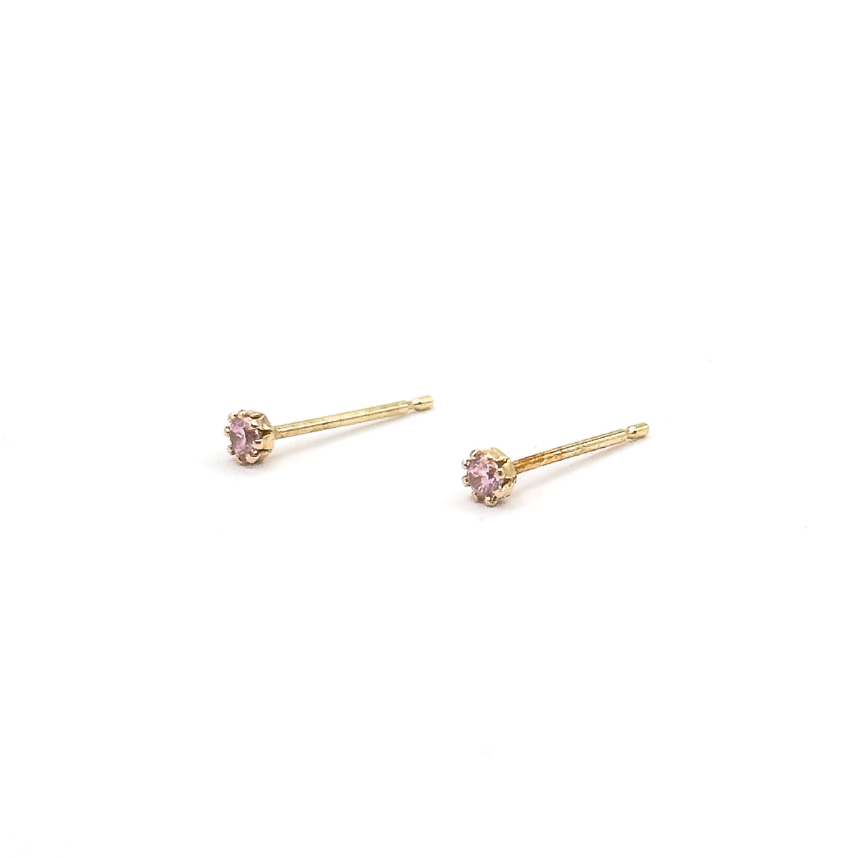 Both studs lie on their sides angled across a white background, each round pink glass stone gripped in its crown of prongs at the end of a long straight post.