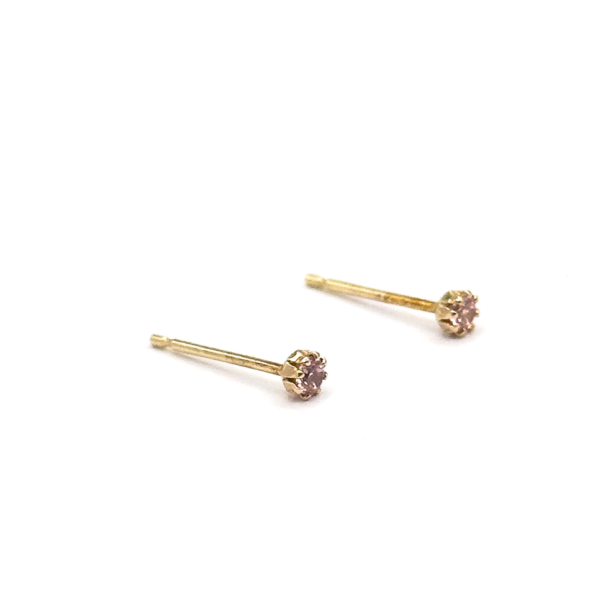 Close in on the two studs lying parallel without their backs, each bare post tapering to a tip while the pink glass stones sit in their prong crowns at the opposite end.