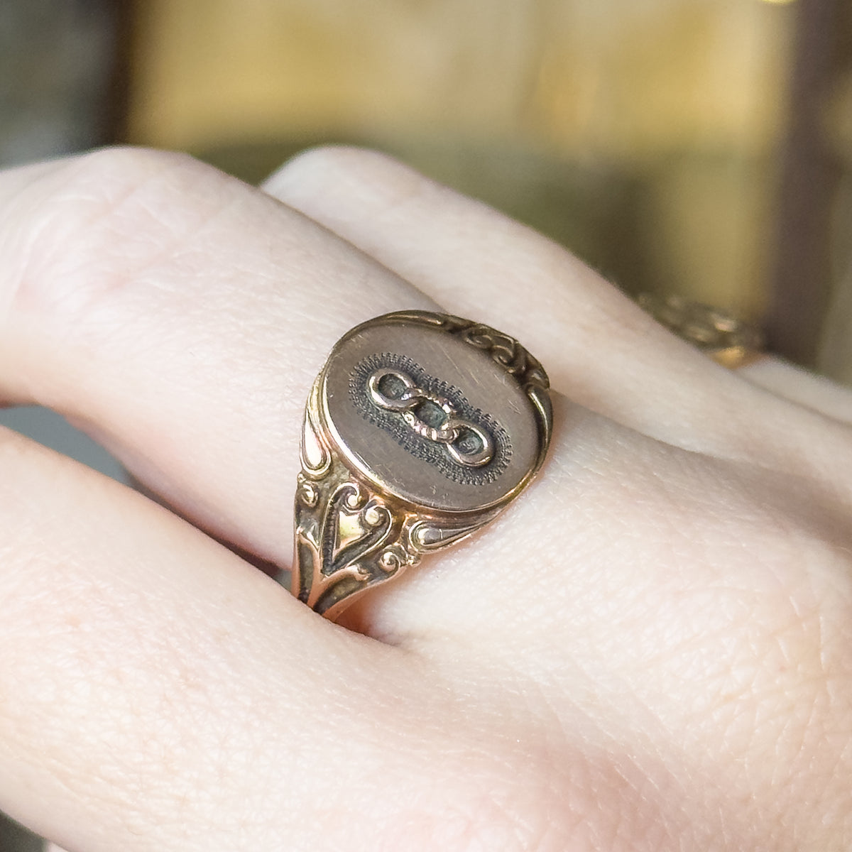 Art Nouveau Odd Fellows signet ring in yellow gold, shown on a finger, its oval face carrying the three-link emblem above scrolled shoulders that taper into a narrow shank.