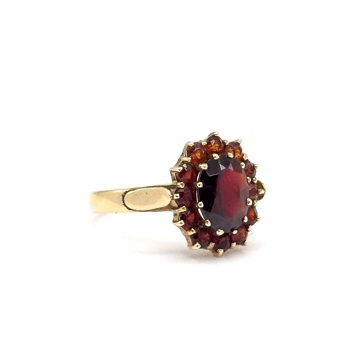 Side-on view against a plain white background, the oval garnet and its prong-set halo raised above the flat tapering shank of yellow gold.
