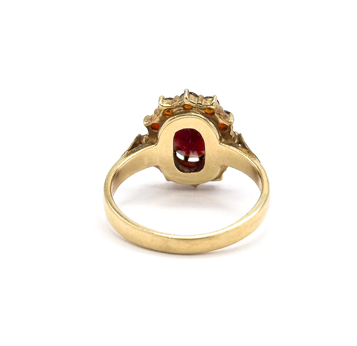 Almost the same view with slightly different angle, looking straight through the shank into the open back of the setting, where the oval garnet glows red between the yellow gold walls.