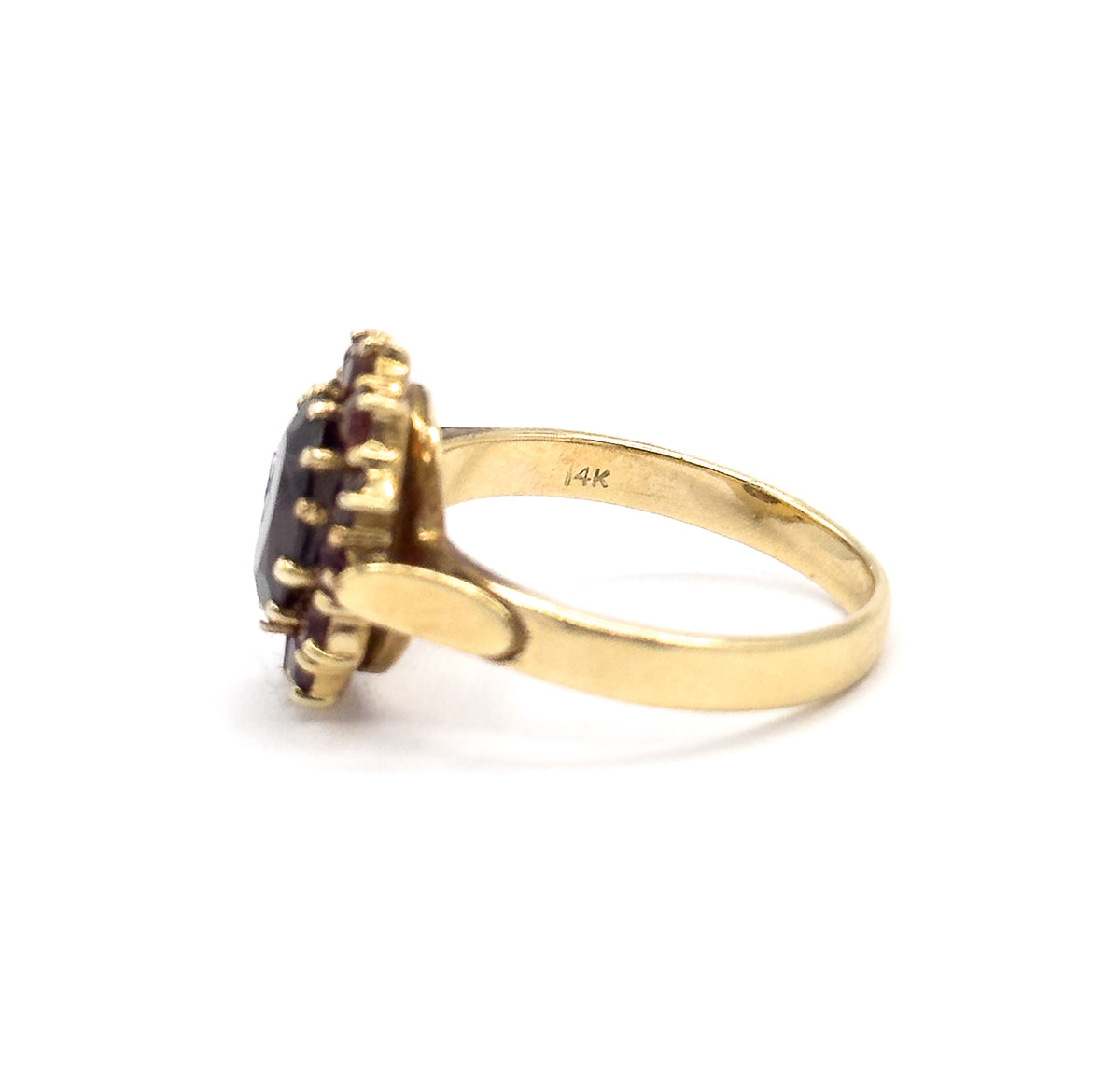 Profile view from the back with the inside of the yellow gold shank turned to the light, a small stamp visible on the band and the prong-set garnet halo in silhouette at the left.