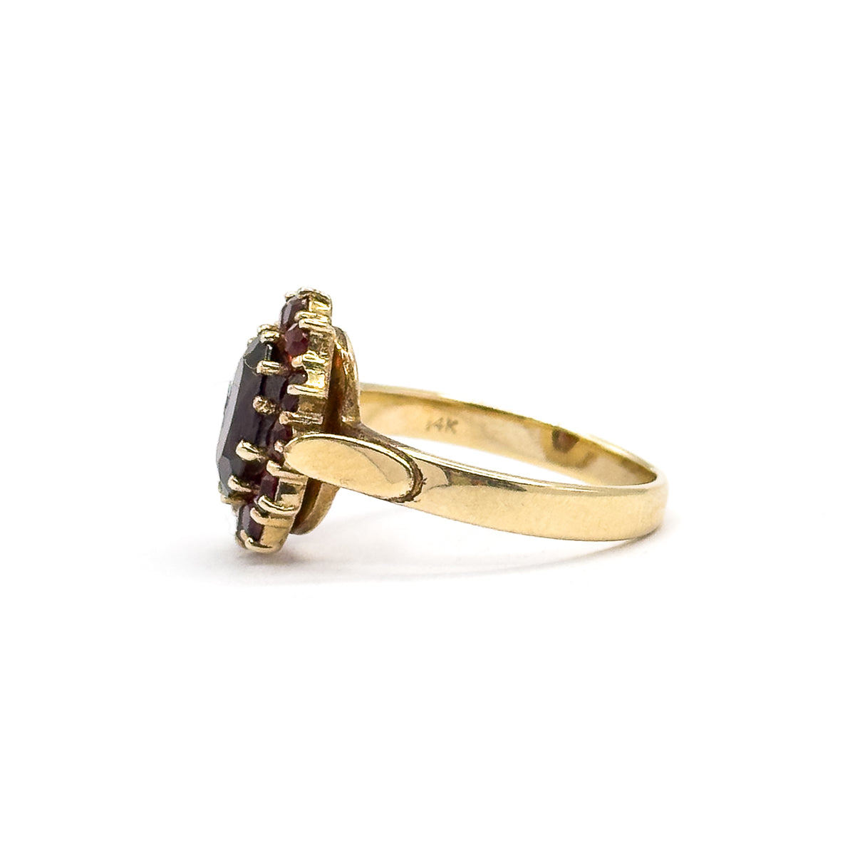 Side profile with the shank sweeping to the right, showing how high the garnet cluster sits above the band and the row of prongs gripping the small round stones along its edge.