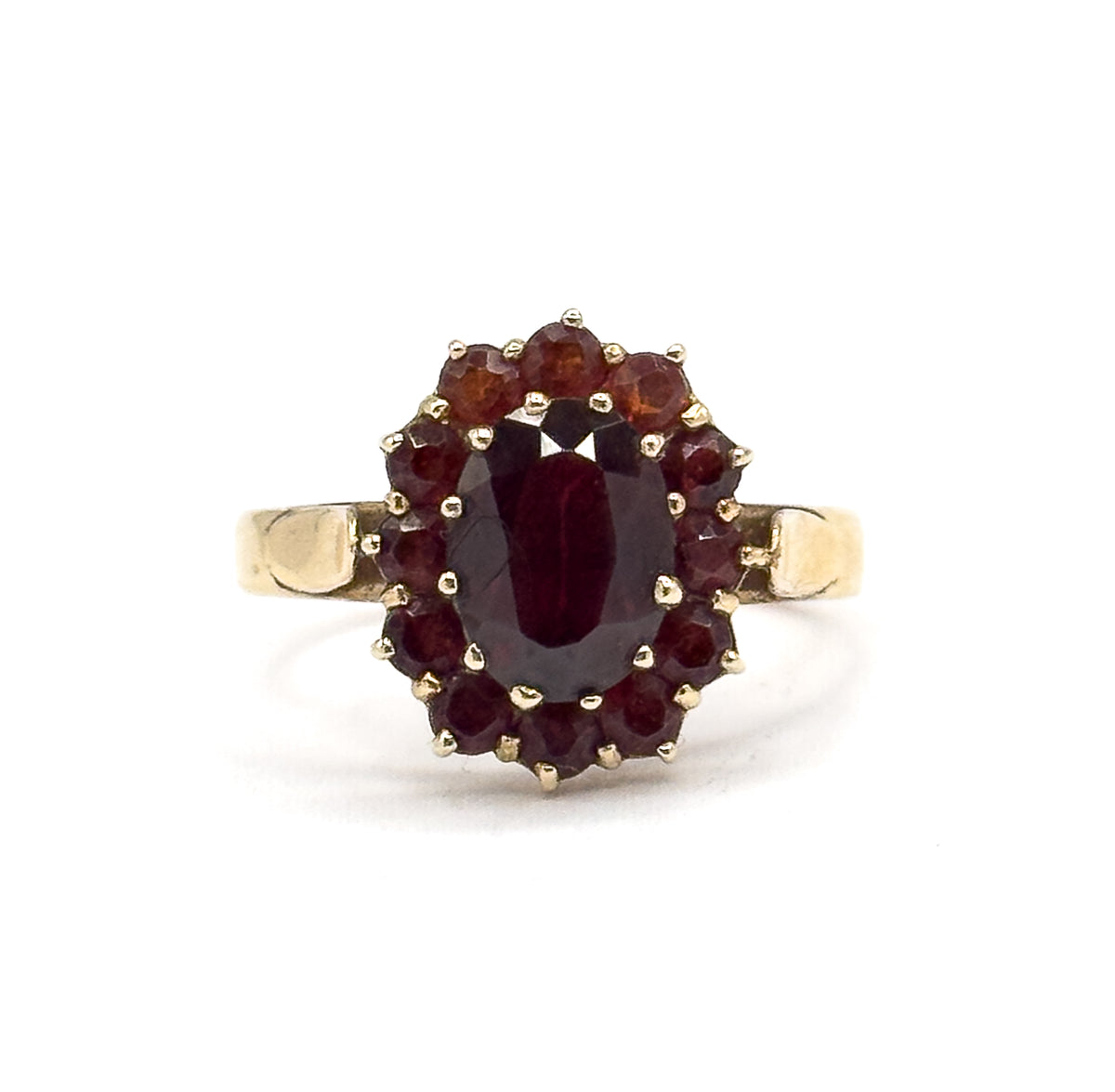 Face-on view against white with the ring upright, the oval garnet centred in its prong-set bezel inside a full ring of twelve small round garnets and squared yellow gold shoulders either side.