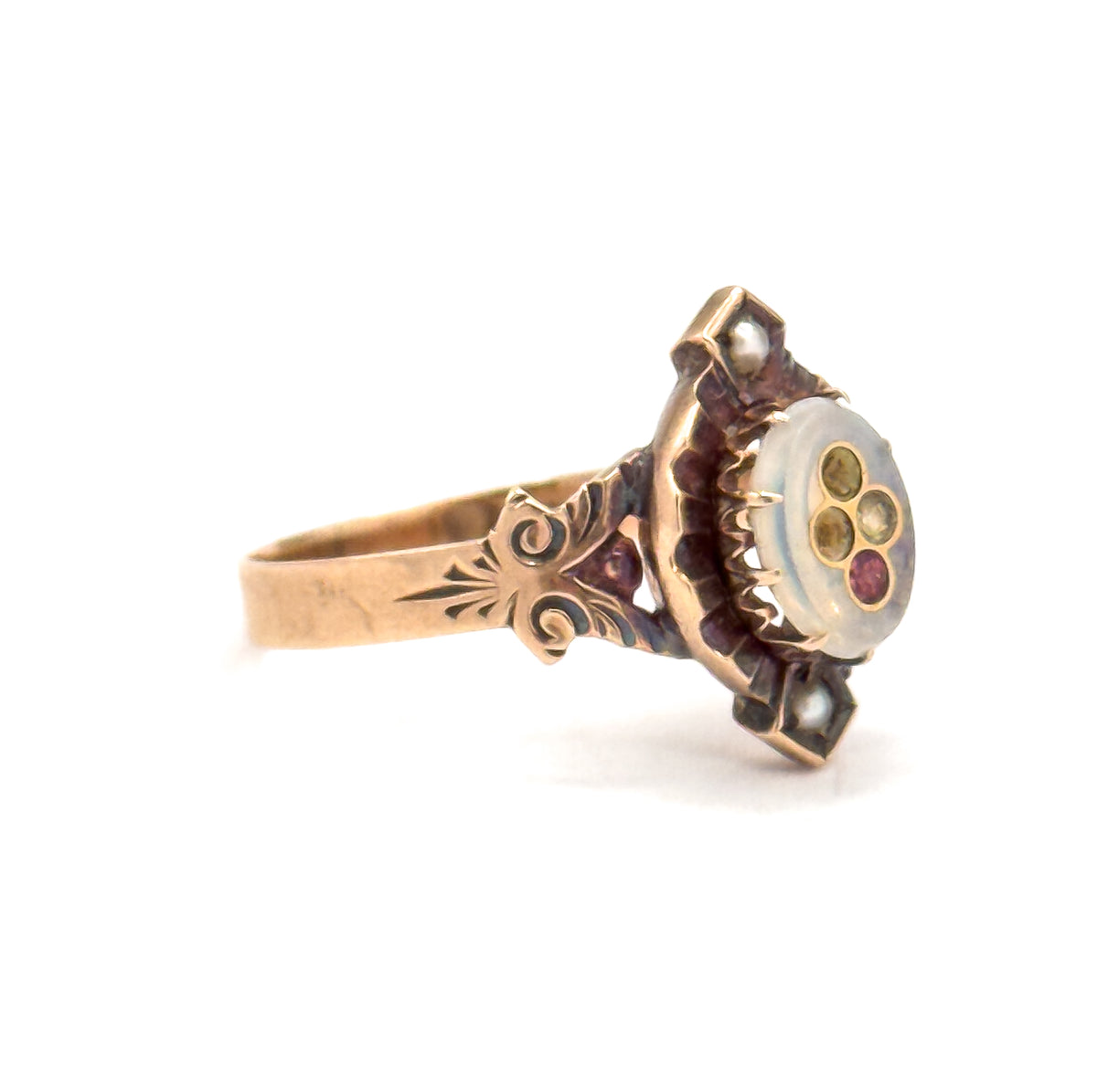 Angled from the side against white, the raised oval face turns toward the lens so the milky glass paste centre with its small pink and colourless inlays sits above prongs and engraved shoulders.
