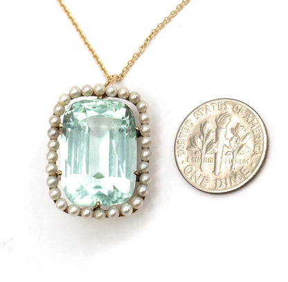 Face-up on white beside a US dime for scale, the pendant only slightly taller than the coin, its seafoam aquamarine and seed pearl halo above the yellow gold chain rising to the top edge.
