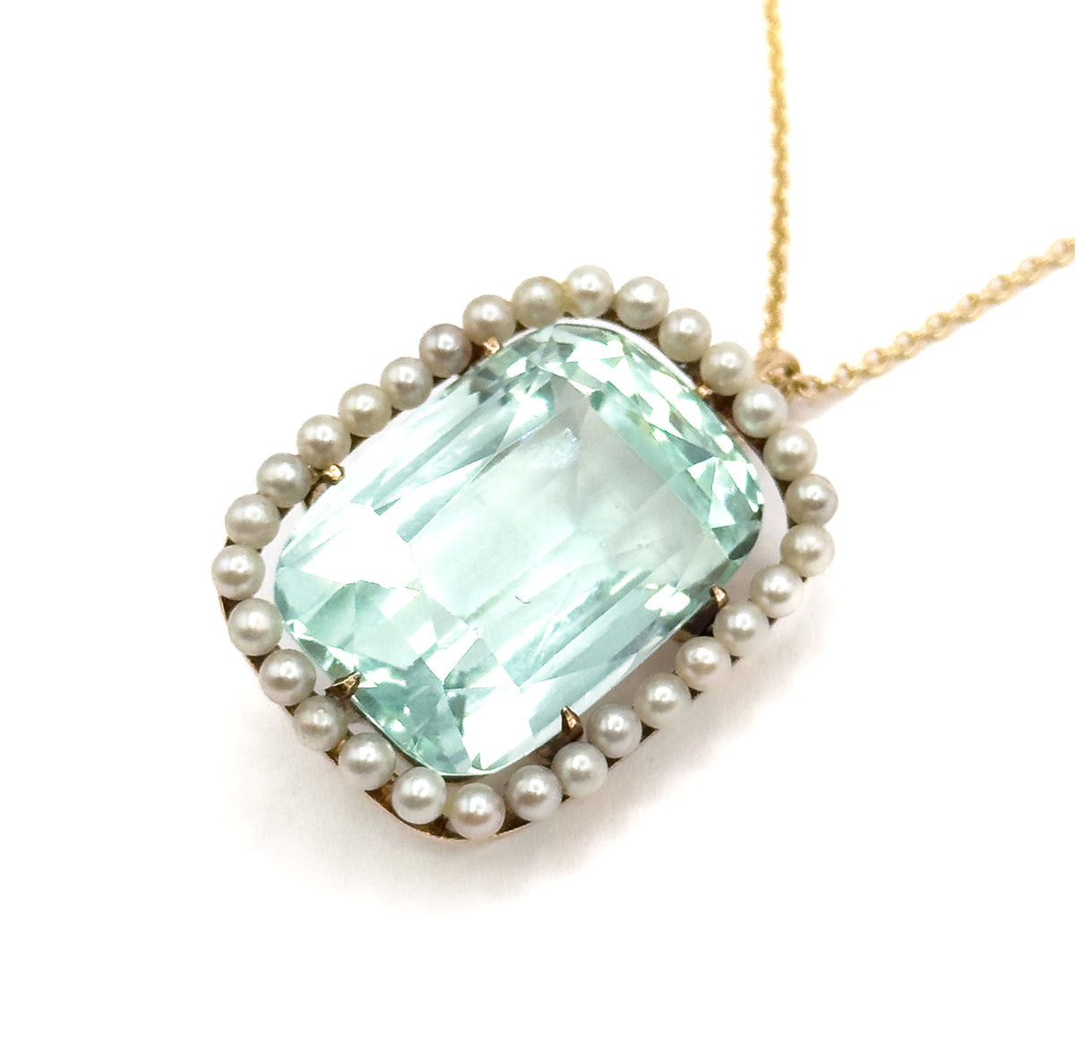 Angled three-quarter view tipping the pendant towards the viewer, showing the depth of the gold basket under the aquamarine and the pearls standing proud of the rim, chain running to upper right.