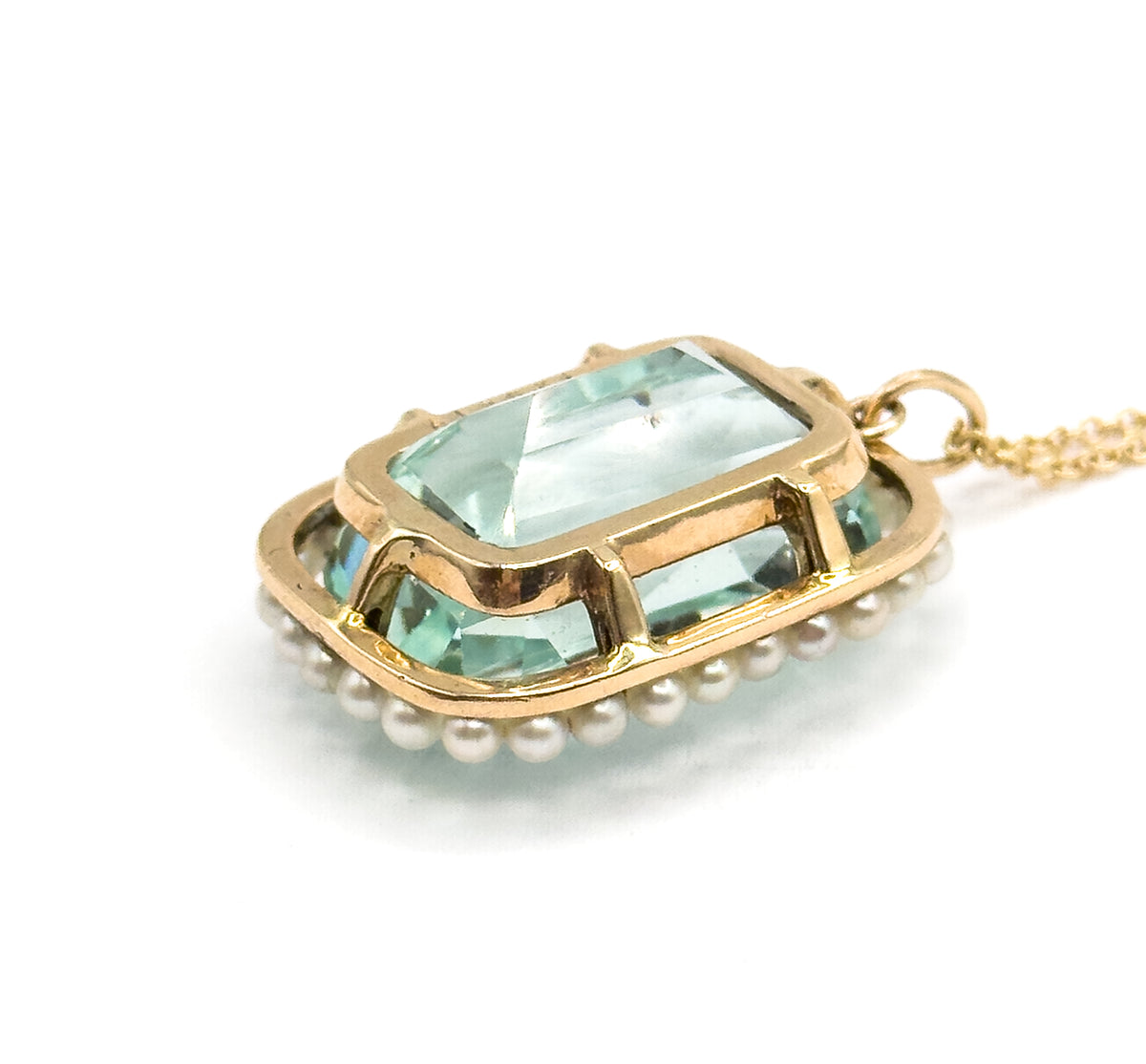Angled three-quarter view on white, the open basket gallery visible from the side with the aquamarine's facets showing through the gold framework and the chain running to the bail.