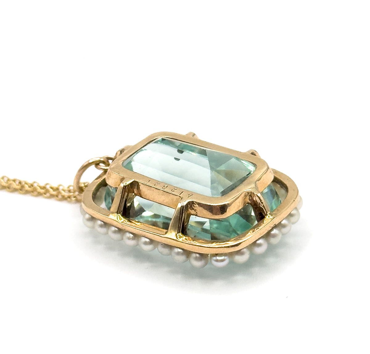 Seen from behind and above, the gold gallery bars cross beneath the aquamarine with a tiny stamp on one bar, the seed pearls ringing the reverse and the chain looping out from the bail.