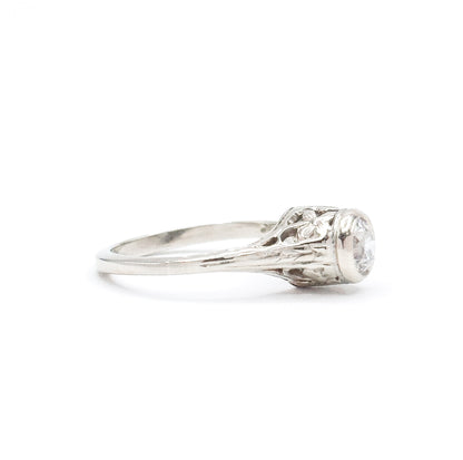 Opposite side profile with the slim shank running off to the left, the flower and pierced scrollwork on this shoulder open to the light and the bezel rim seen edge-on around the diamond.