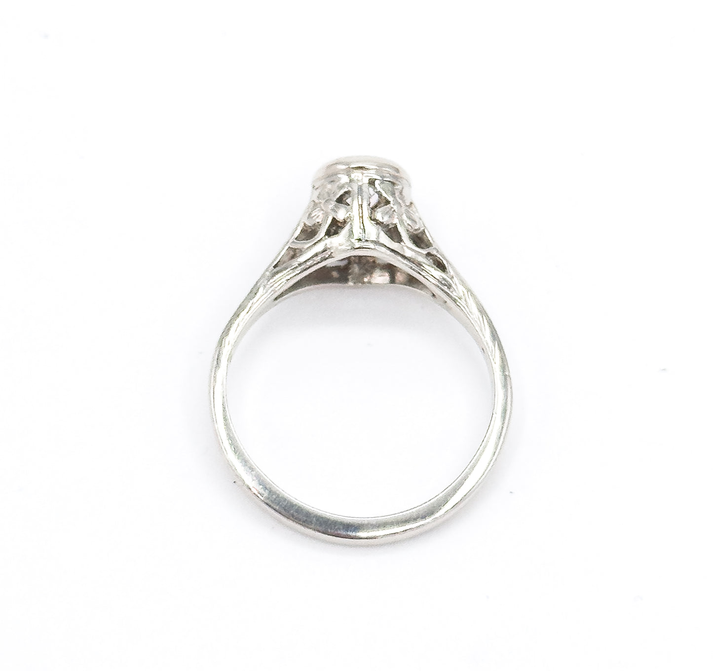 Head-on view down through the open shank, the round white gold band framing the pierced filigree gallery and the underside of the high bezel with the diamond just visible at the top.