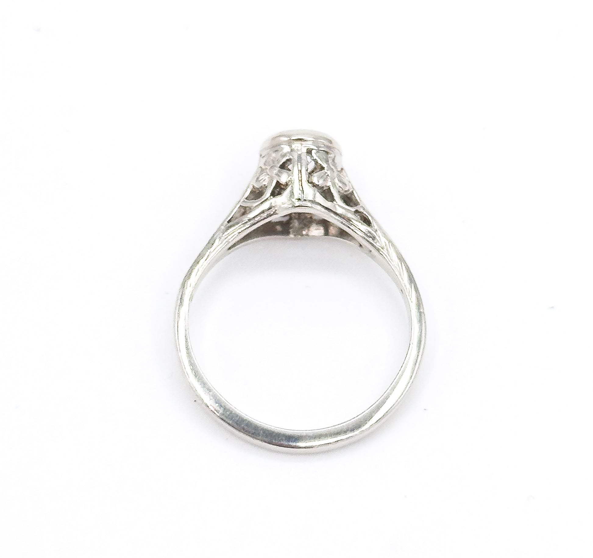 Head-on view down through the open shank, the round white gold band framing the pierced filigree gallery and the underside of the high bezel with the diamond just visible at the top.