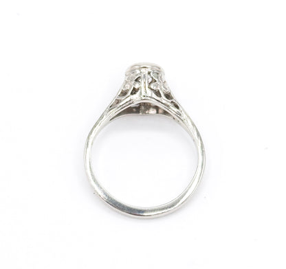 Head-on view down through the open shank, the round white gold band framing the pierced filigree gallery and the underside of the high bezel with the diamond just visible at the top.