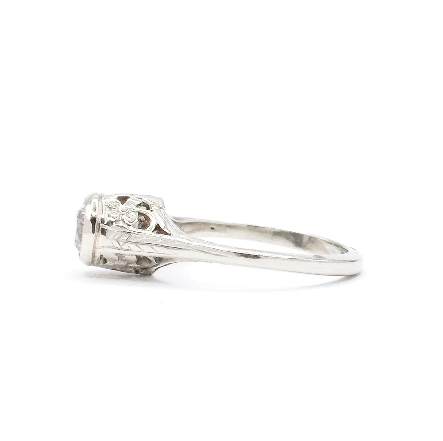 Side profile against white with the shank curving away to the right, showing the chevron engraving along the tapered shoulder and the diamond's edge peeking past the bezel.