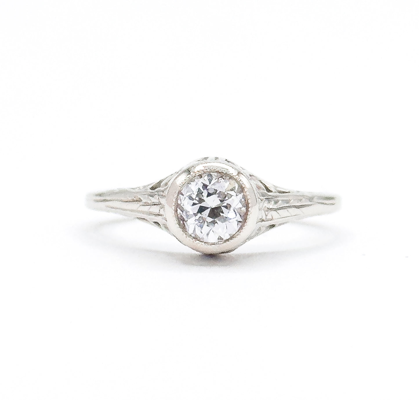 Art Deco old European cut diamond solitaire ring in white gold, shown face-on against a plain white background, the bezel-set stone raised high above engraved filigree shoulders and a split shank.