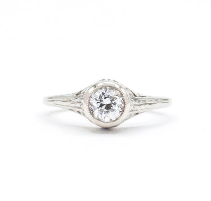 Art Deco old European cut diamond solitaire ring in white gold, shown face-on against a plain white background, the bezel-set stone raised high above engraved filigree shoulders and a split shank.