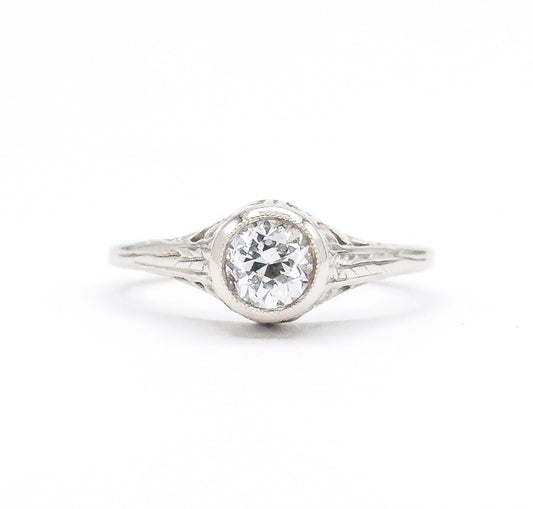 Art Deco old European cut diamond solitaire ring in white gold, shown face-on against a plain white background, the bezel-set stone raised high above engraved filigree shoulders and a split shank.