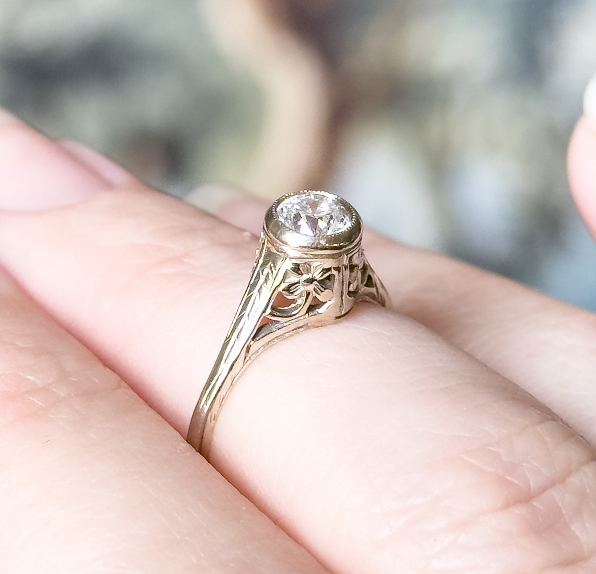 Shown on a finger from the side in close crop, the high bezel and pierced flower shoulder standing clear of the skin, the slim shank spanning barely a fifth of the finger's length.