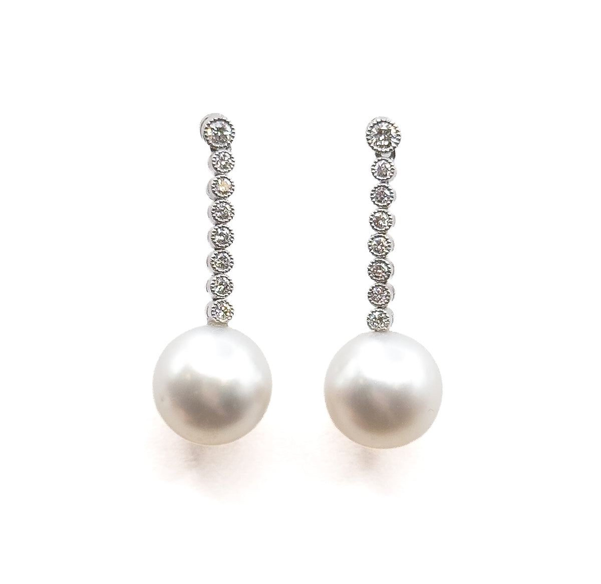 Straight-on and upright, the pair standing parallel so the round bezel-set diamonds read as an even column down each line, ending in the two round pearl drops with soft shadow below.