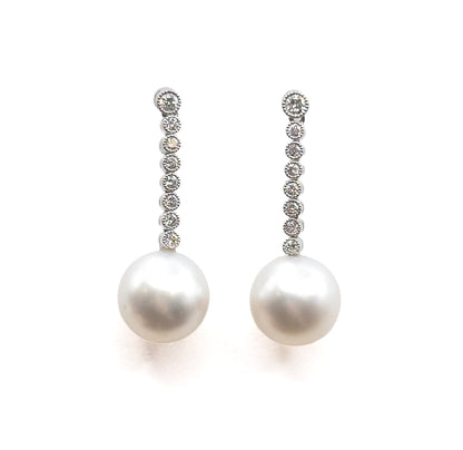 Straight-on and upright, the pair standing parallel so the round bezel-set diamonds read as an even column down each line, ending in the two round pearl drops with soft shadow below.