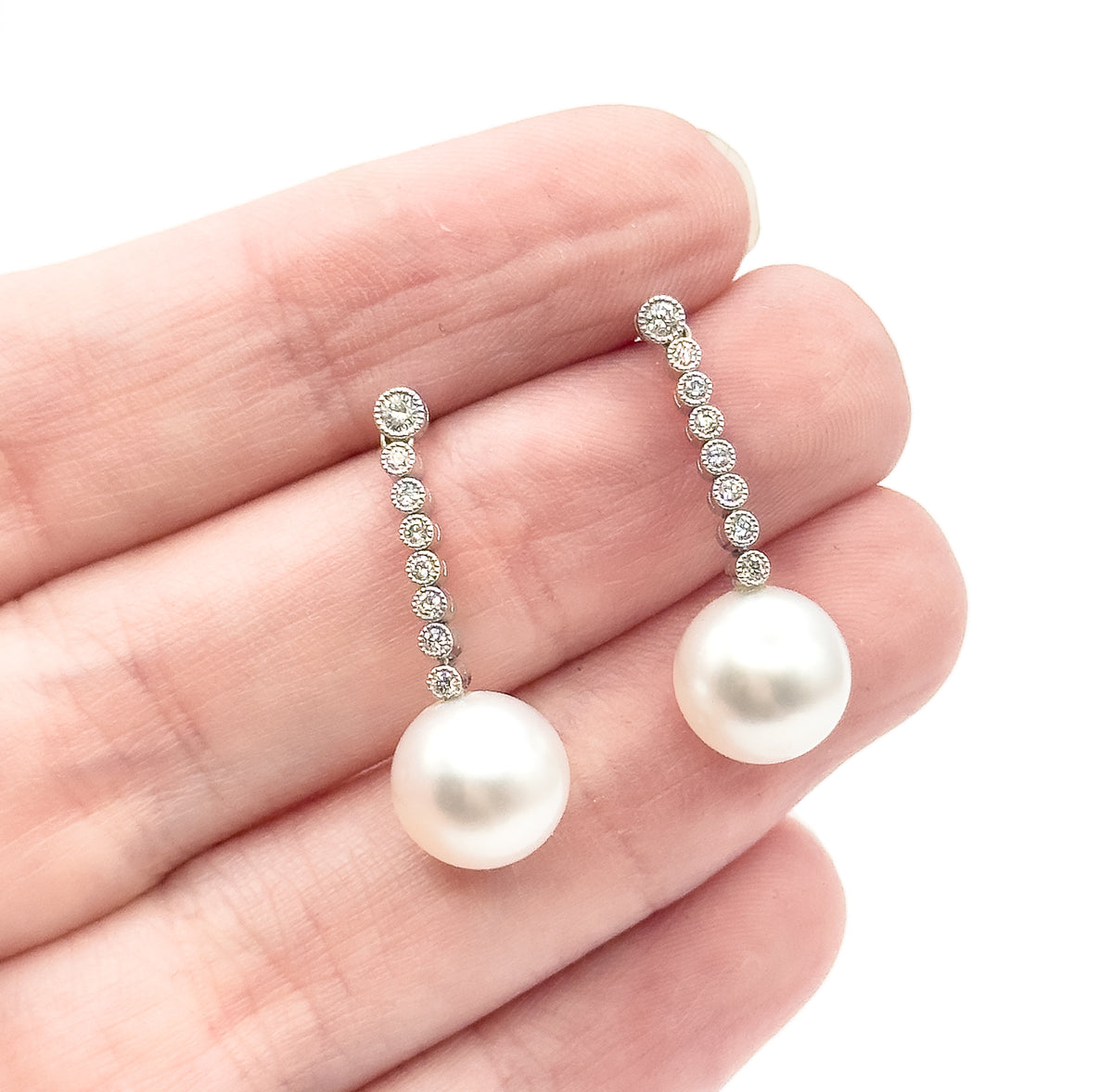 Both earrings resting across the fingers of an open palm, giving a sense of scale: each graduated diamond line is about a fingertip long, with the creamy pearl drop below.