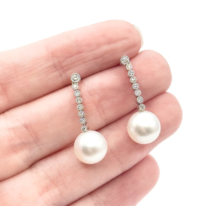 Both earrings resting across the fingers of an open palm, giving a sense of scale: each graduated diamond line is about a fingertip long, with the creamy pearl drop below.